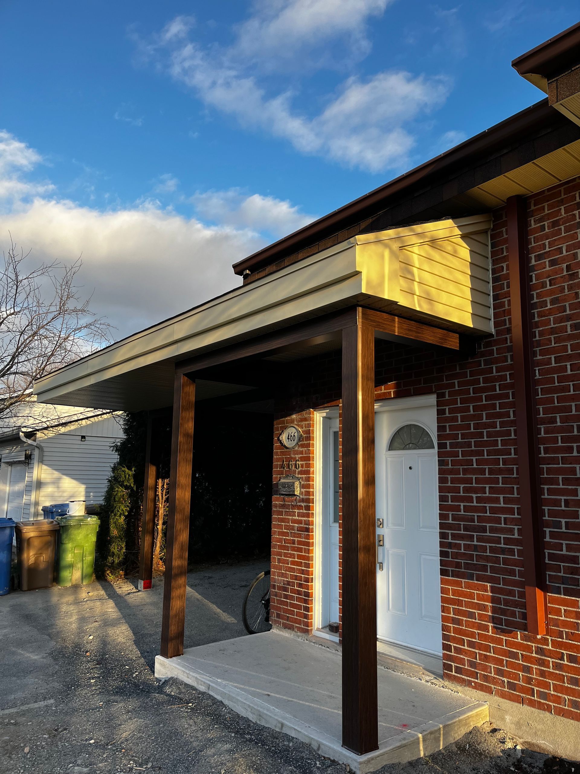 Auvent à cadre marron au-dessus d'une porte blanche sur un bâtiment en briques avec une allée en béton.