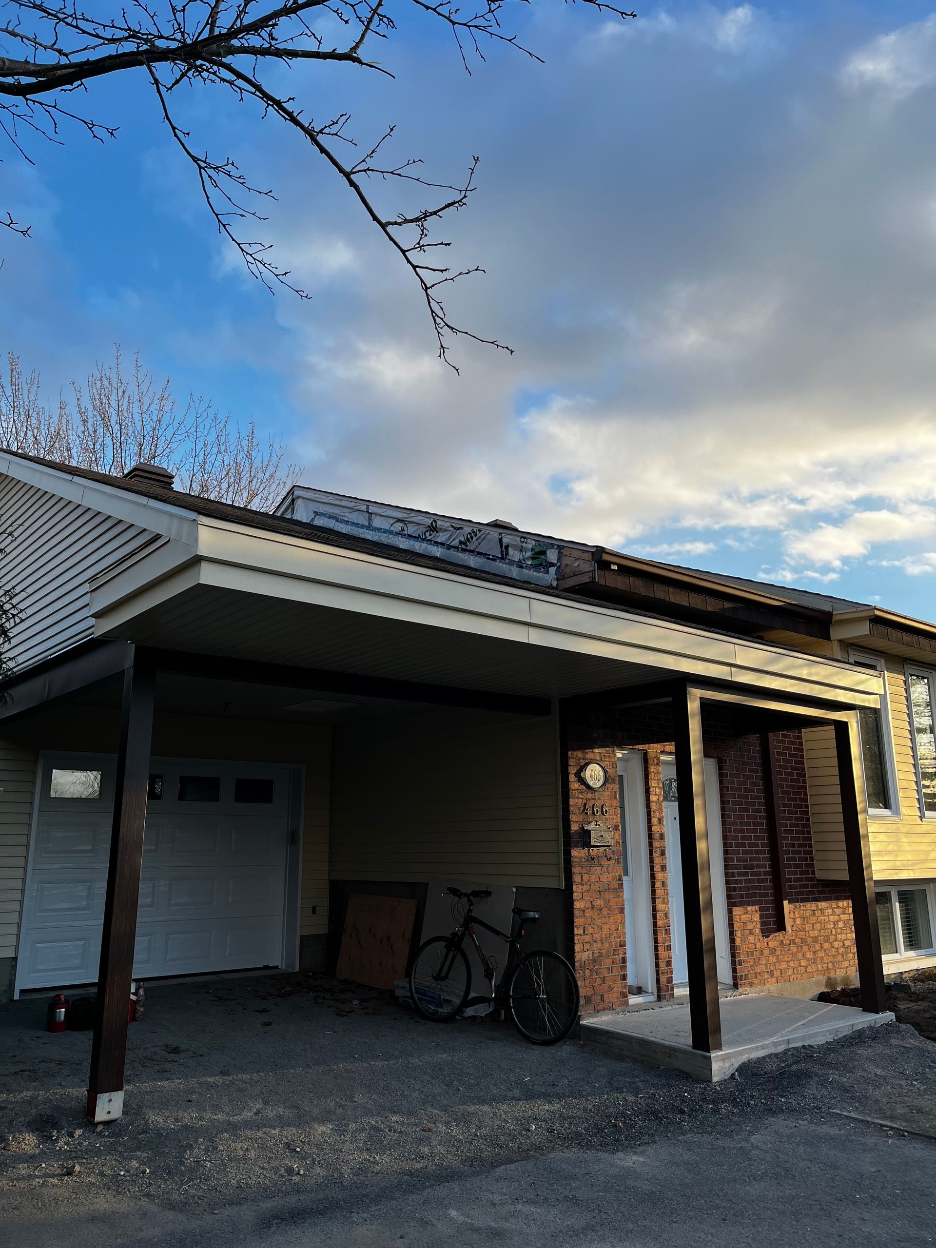 Extérieur de la maison avec panneaux solaires sur le toit, abri voiture et garage. Ciel bleu avec des nuages.