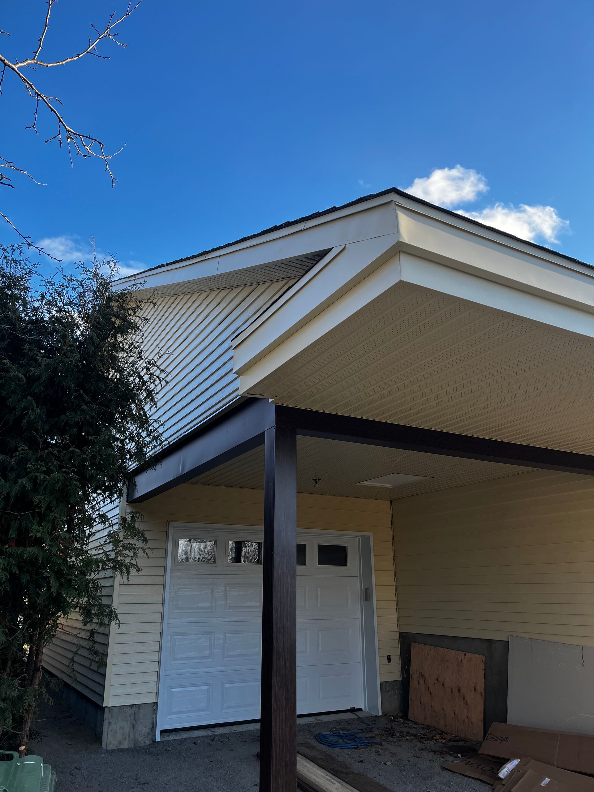 Garage aux portes blanches, bardage beige et boiseries marron, sous un ciel bleu.