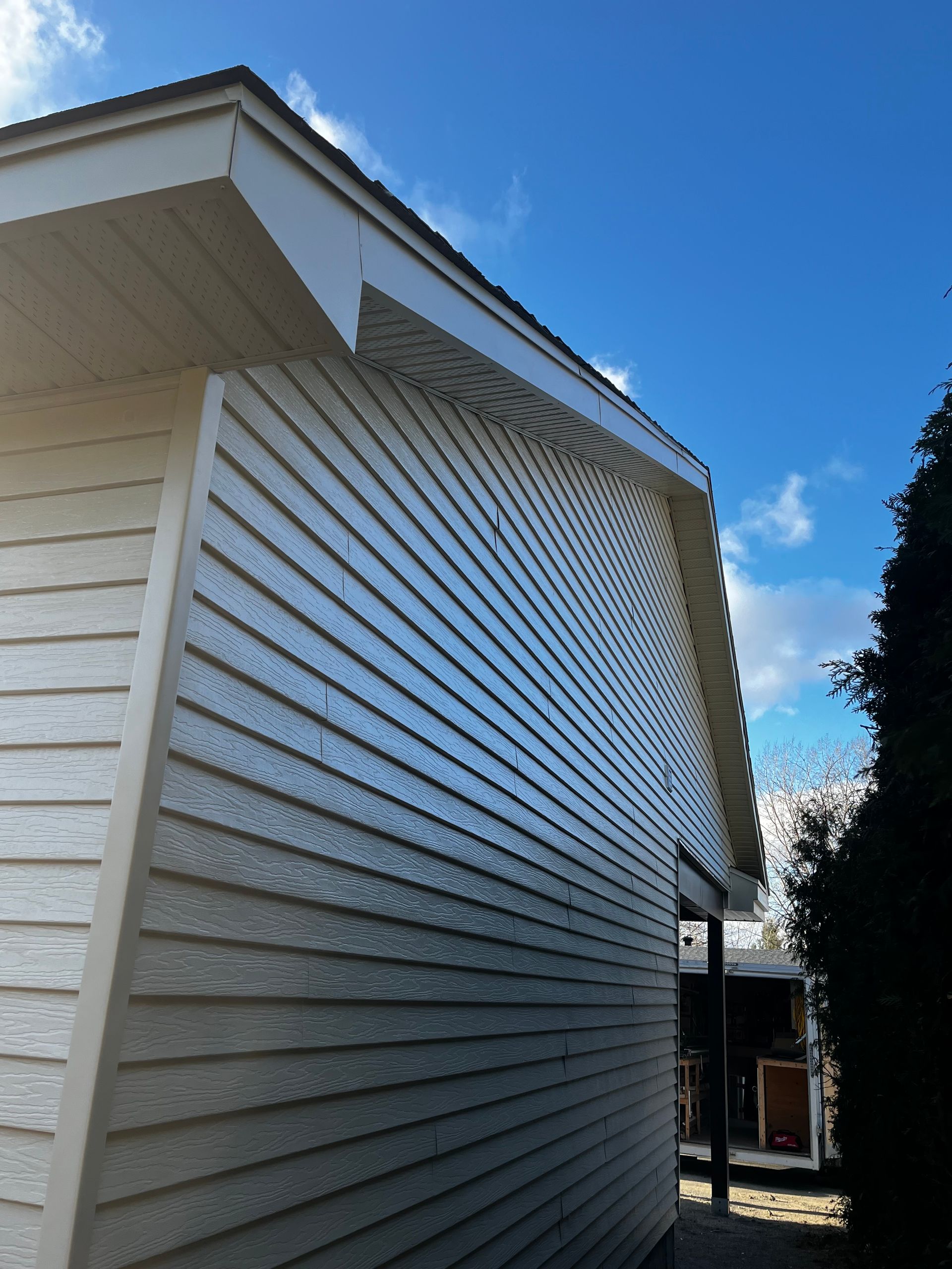 Bardage couleur crème sur un bâtiment au toit et aux boiseries beiges, se détachant sur un ciel bleu nuageux.
