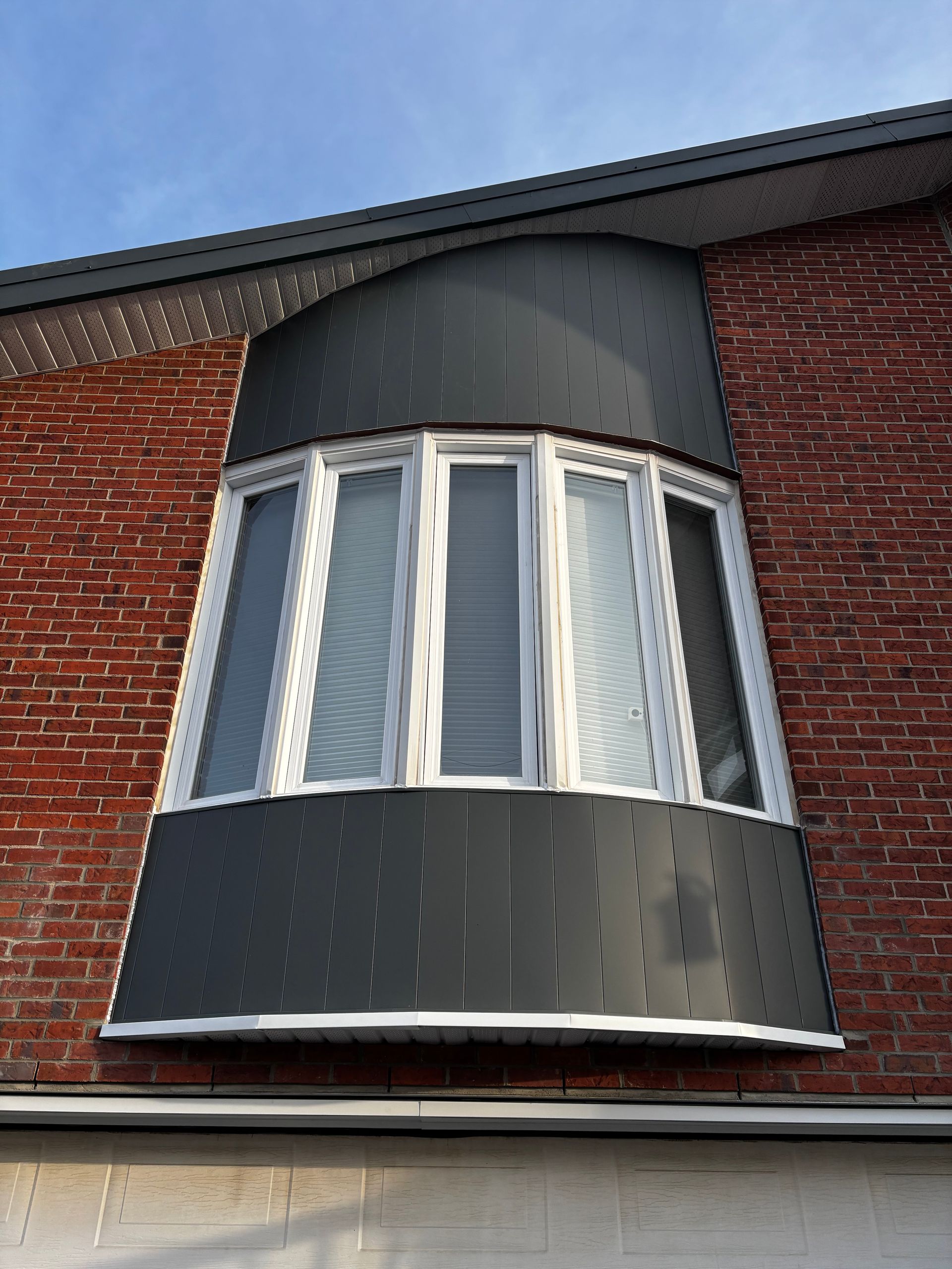 Fenêtre en baie avec panneaux incurvés gris foncé contre un mur de briques.