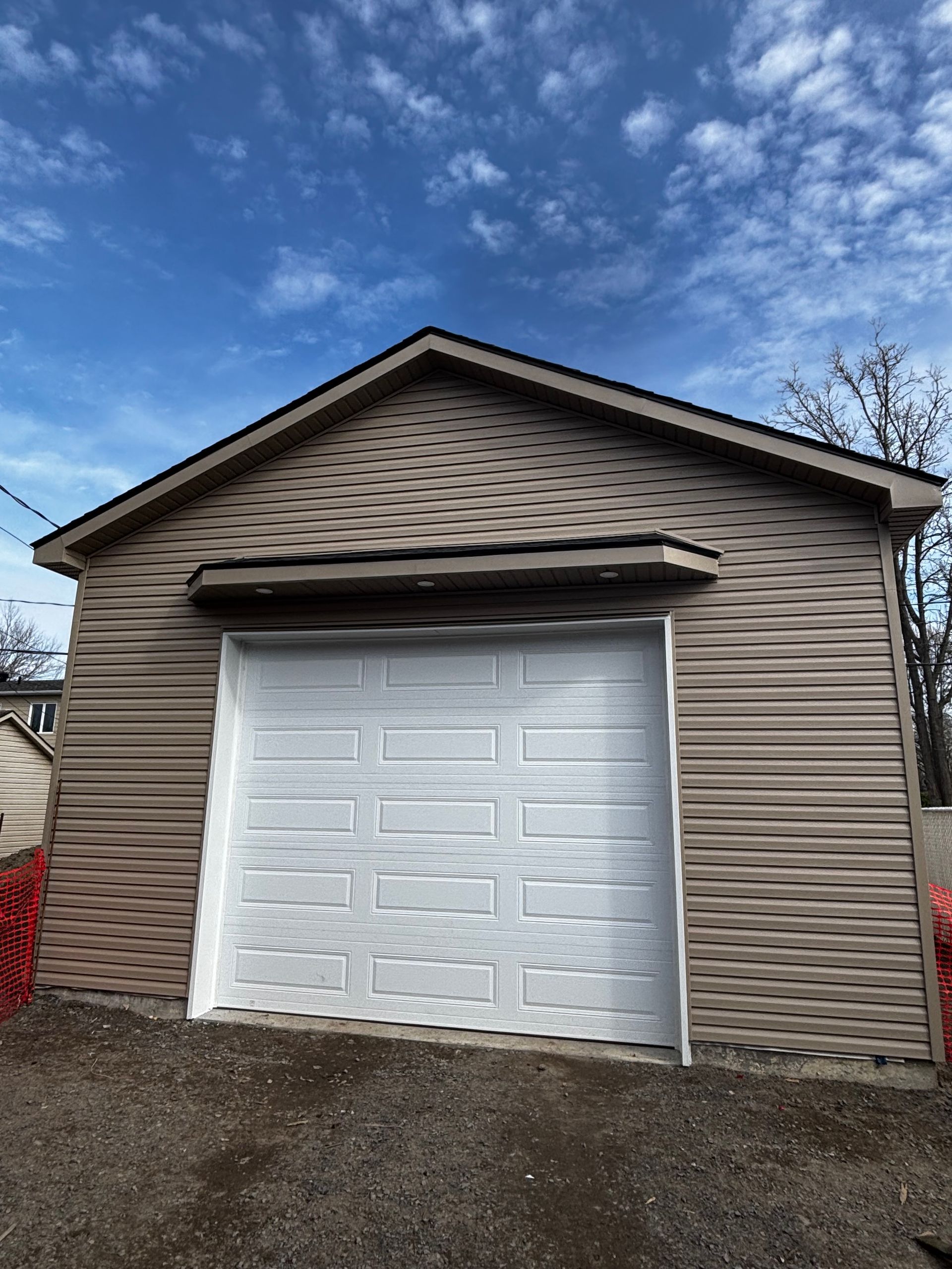 Garage beige avec porte de garage blanche sous un ciel bleu.