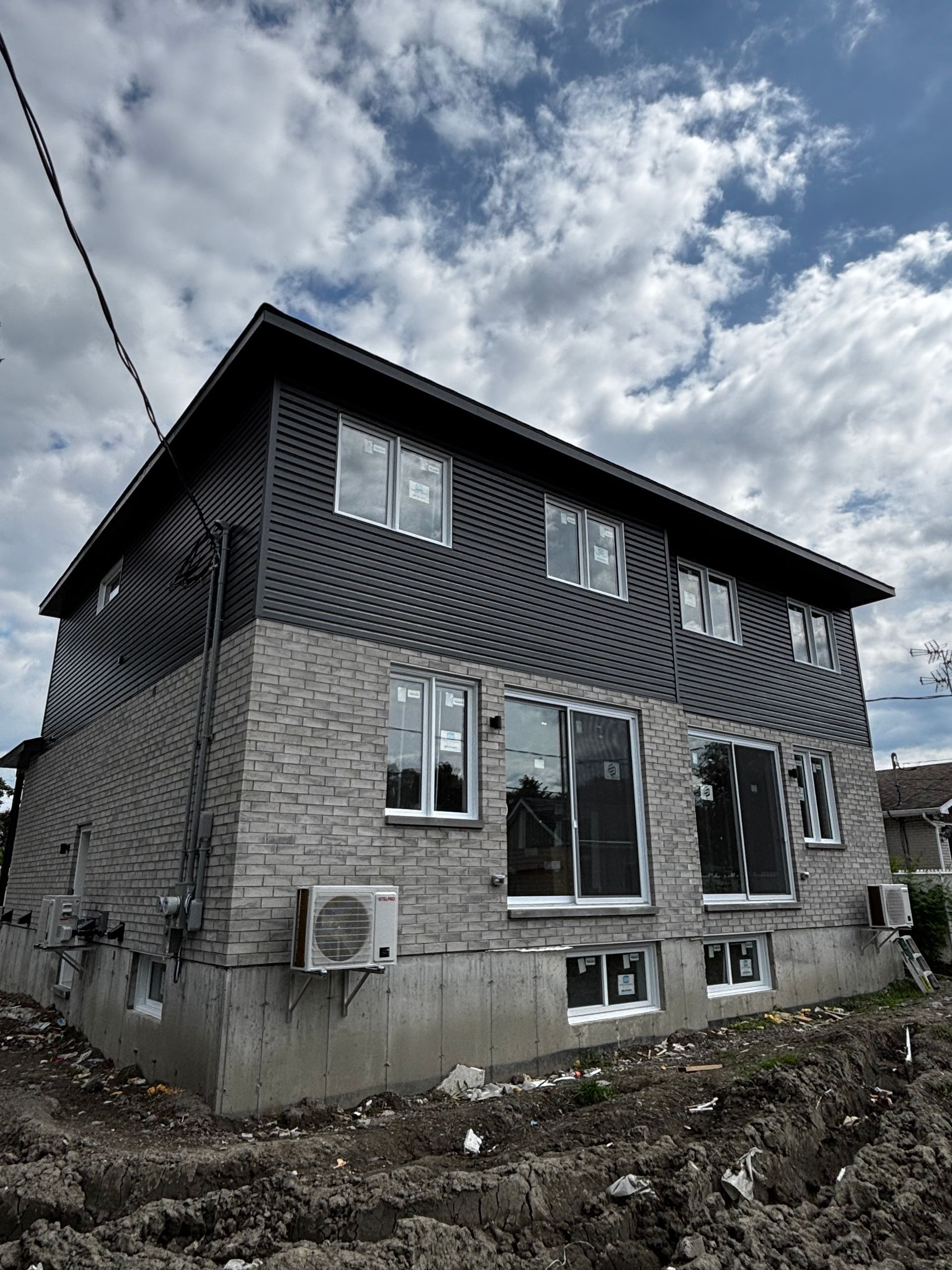 Maison à deux étages en briques avec un revêtement sombre, des fenêtres et un ciel nuageux.