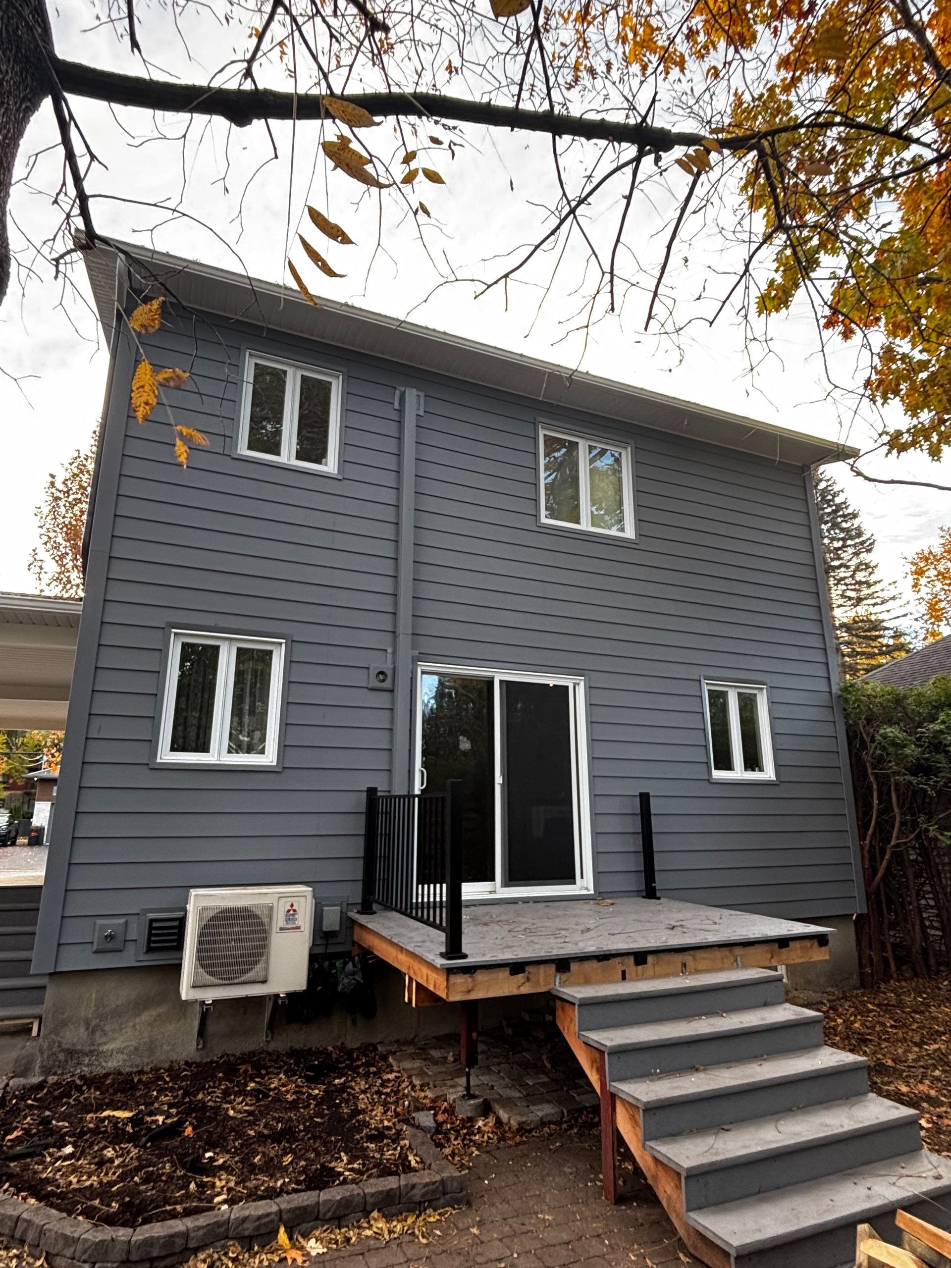 Maison grise à deux étages, fenêtres à cadre blanc, terrasse et escalier extérieur.