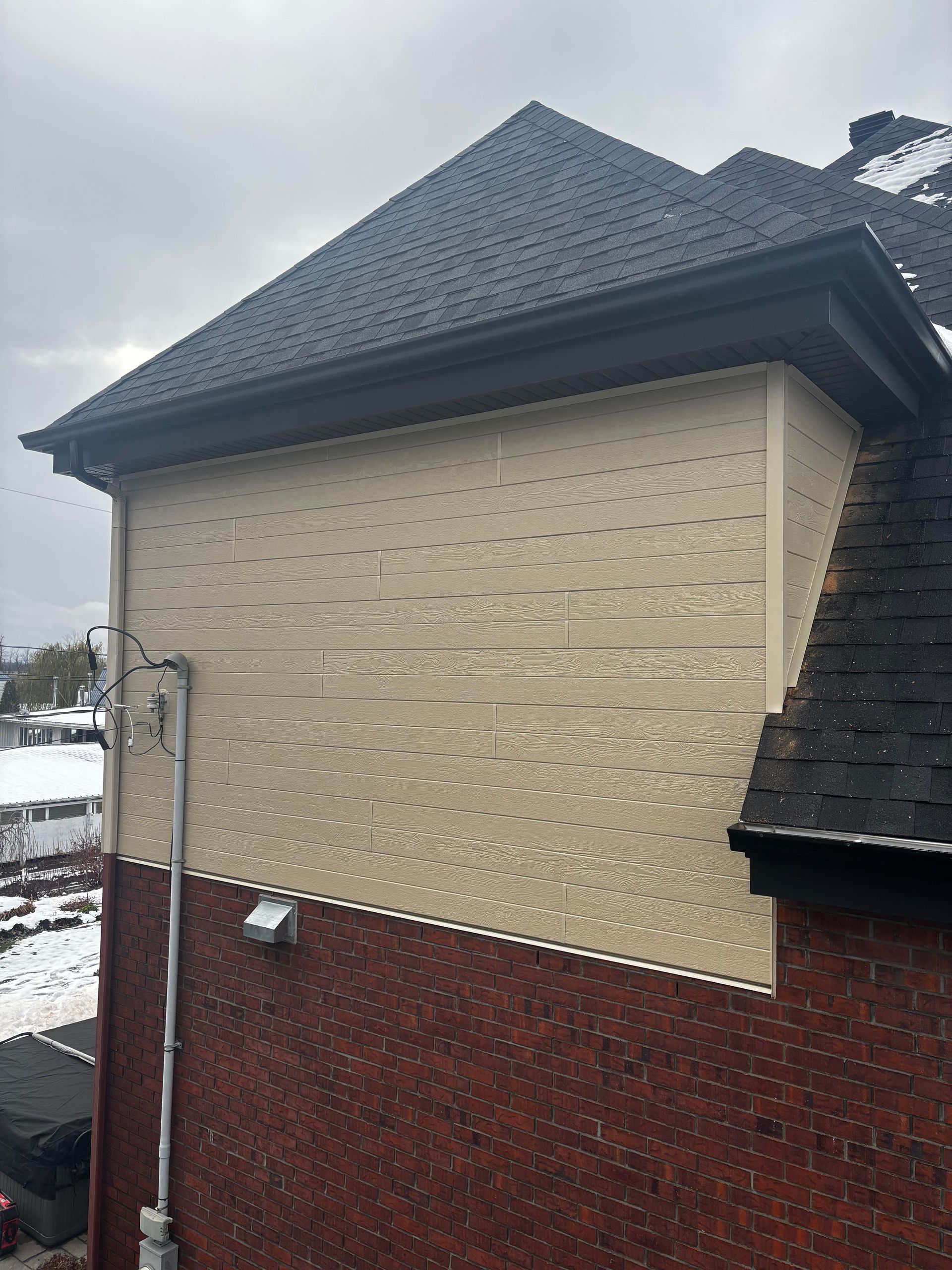 Extérieur d'un bâtiment aux murs de briques et de couleur beige, au toit sombre et sous un ciel couvert.