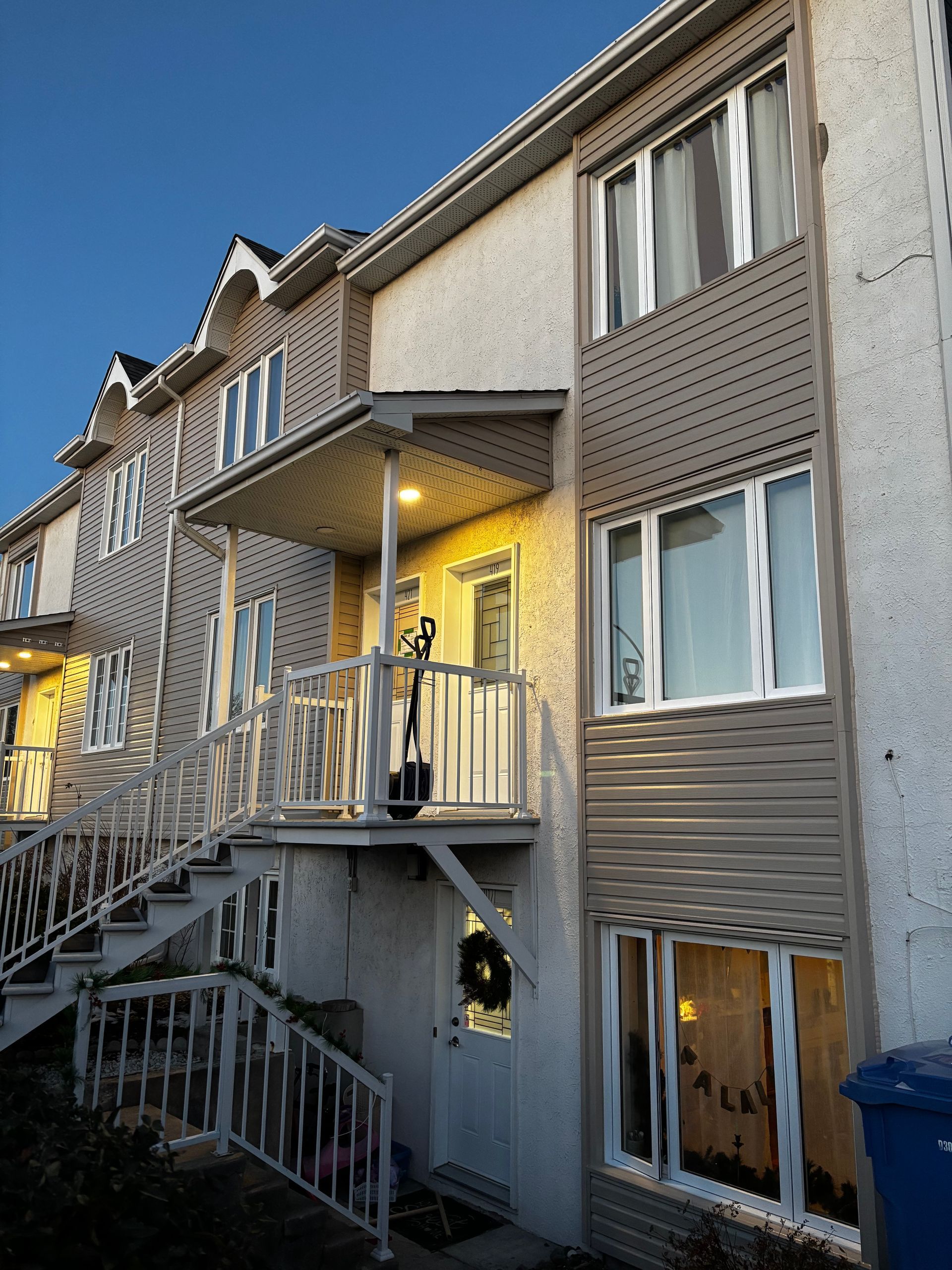 Maisons de ville avec escaliers menant aux entrées, façades beiges et blanches, portes éclairées et ciel bleu.