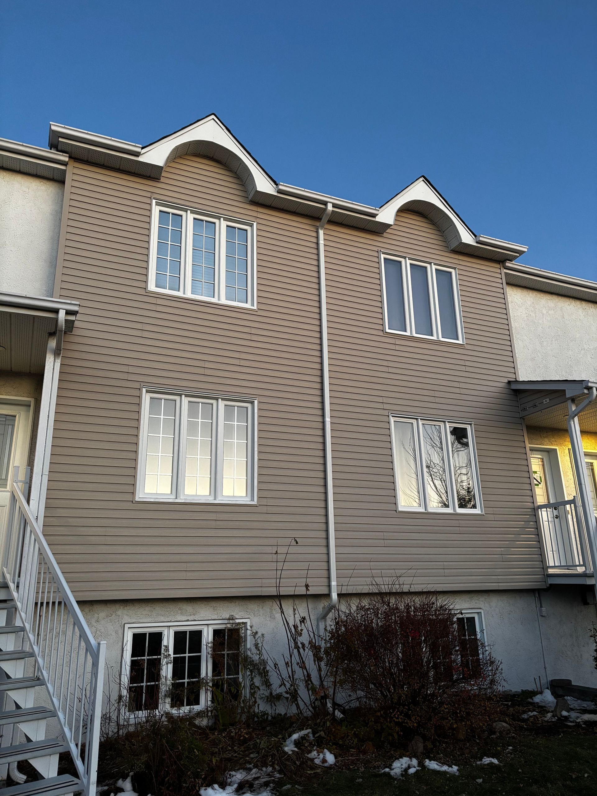 Maison de ville beige avec de nombreuses fenêtres, se détachant sur un ciel bleu. Un escalier mène à une porte blanche sur la droite.