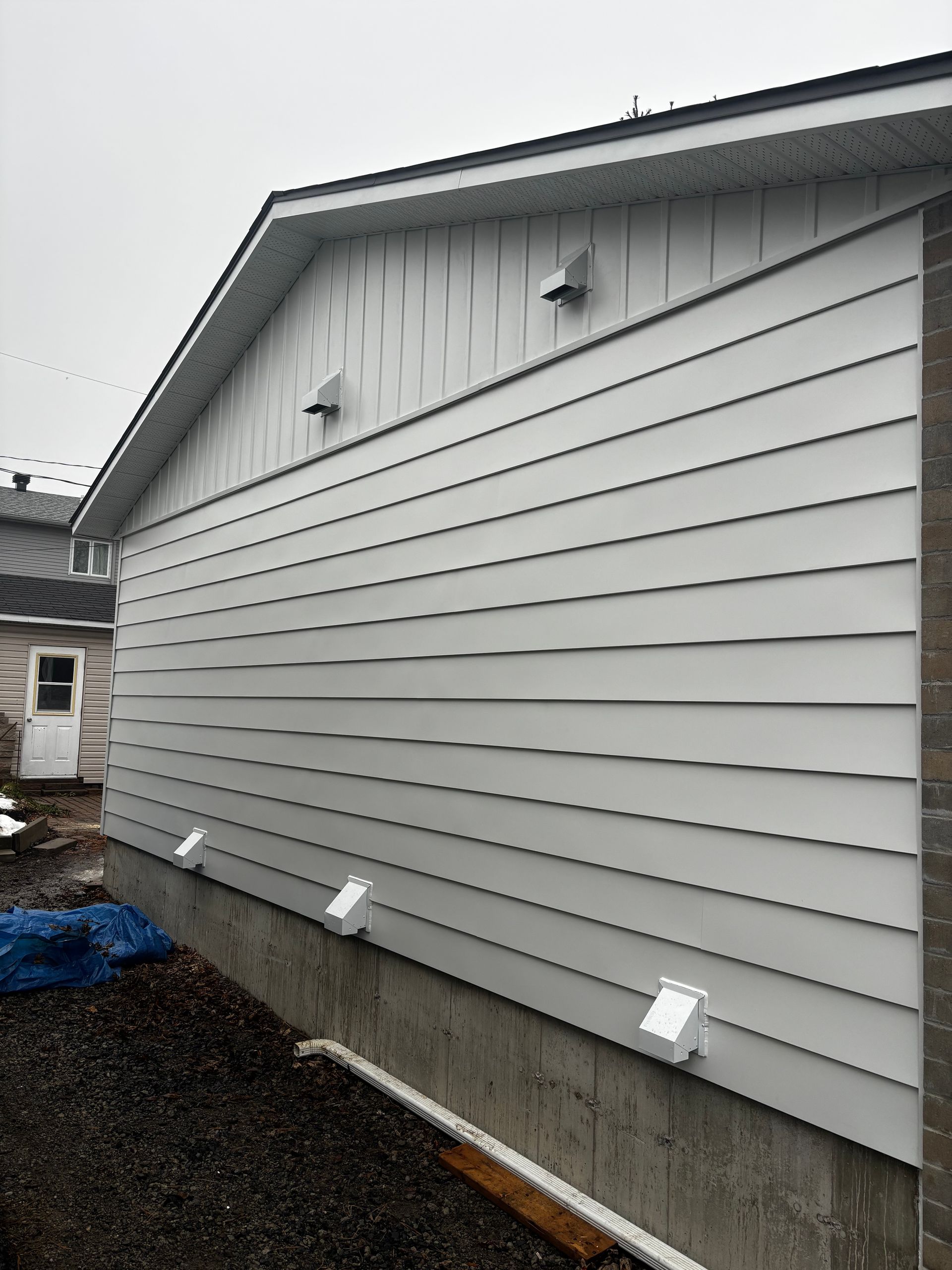 Bâtiment à façade blanche avec des ouvertures d'aération. La façade repose sur des fondations en béton. Une petite porte est visible à l'arrière-plan.