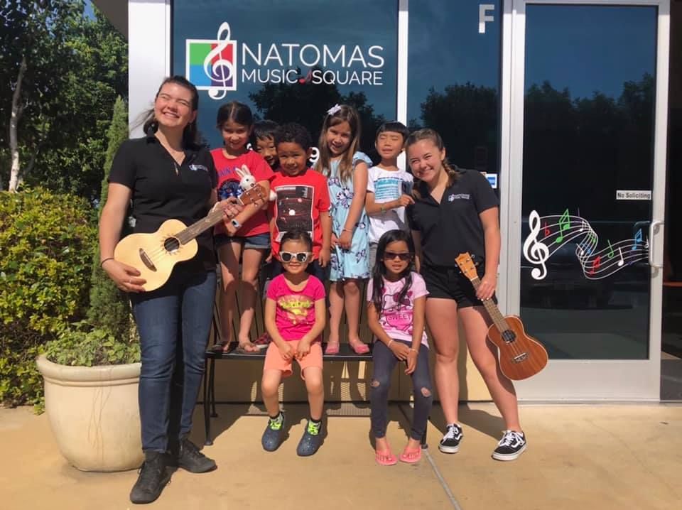 A group of children are posing for a picture with a woman holding a guitar.