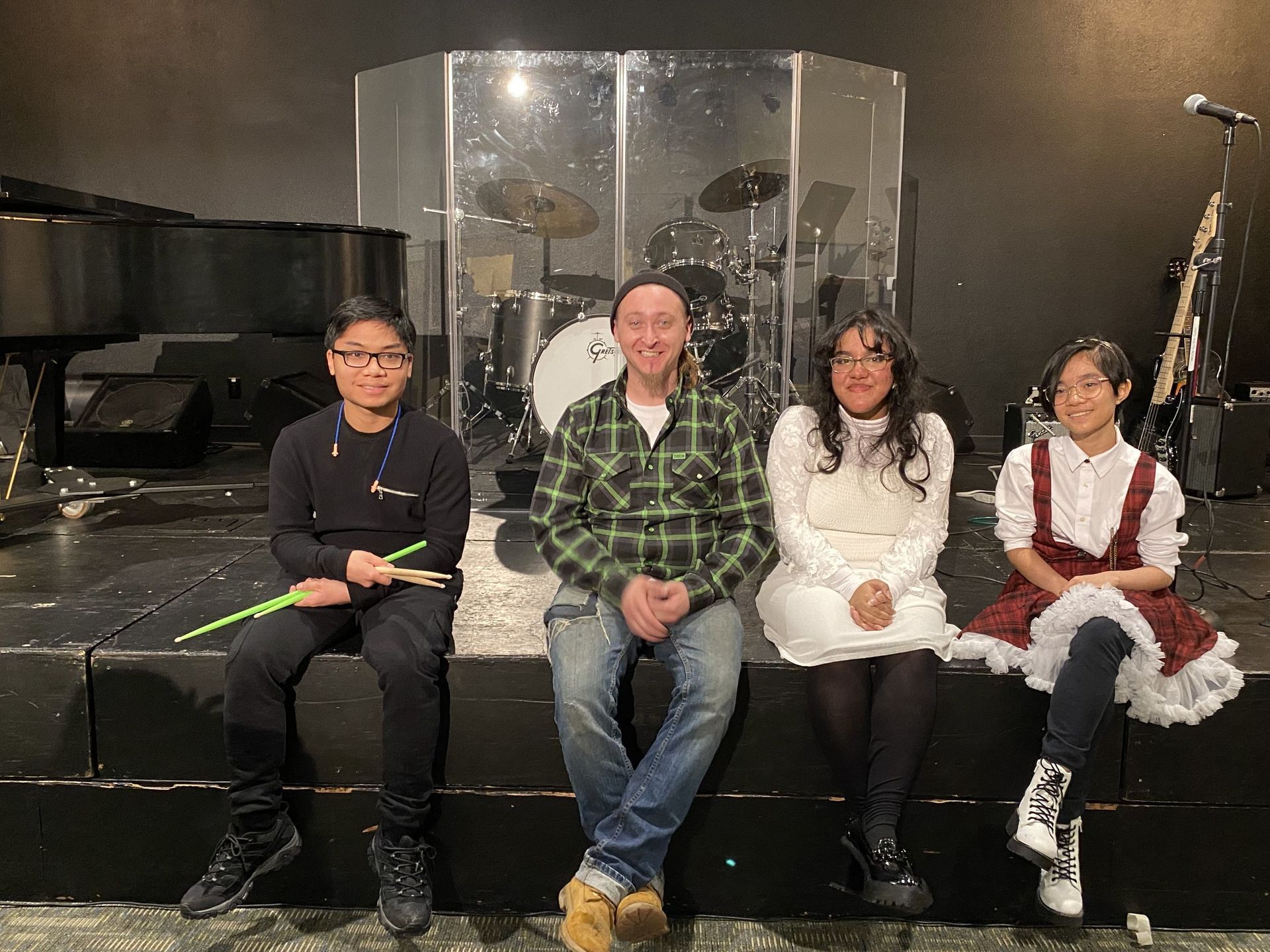 A group of people are sitting on a stage in front of a drum set.