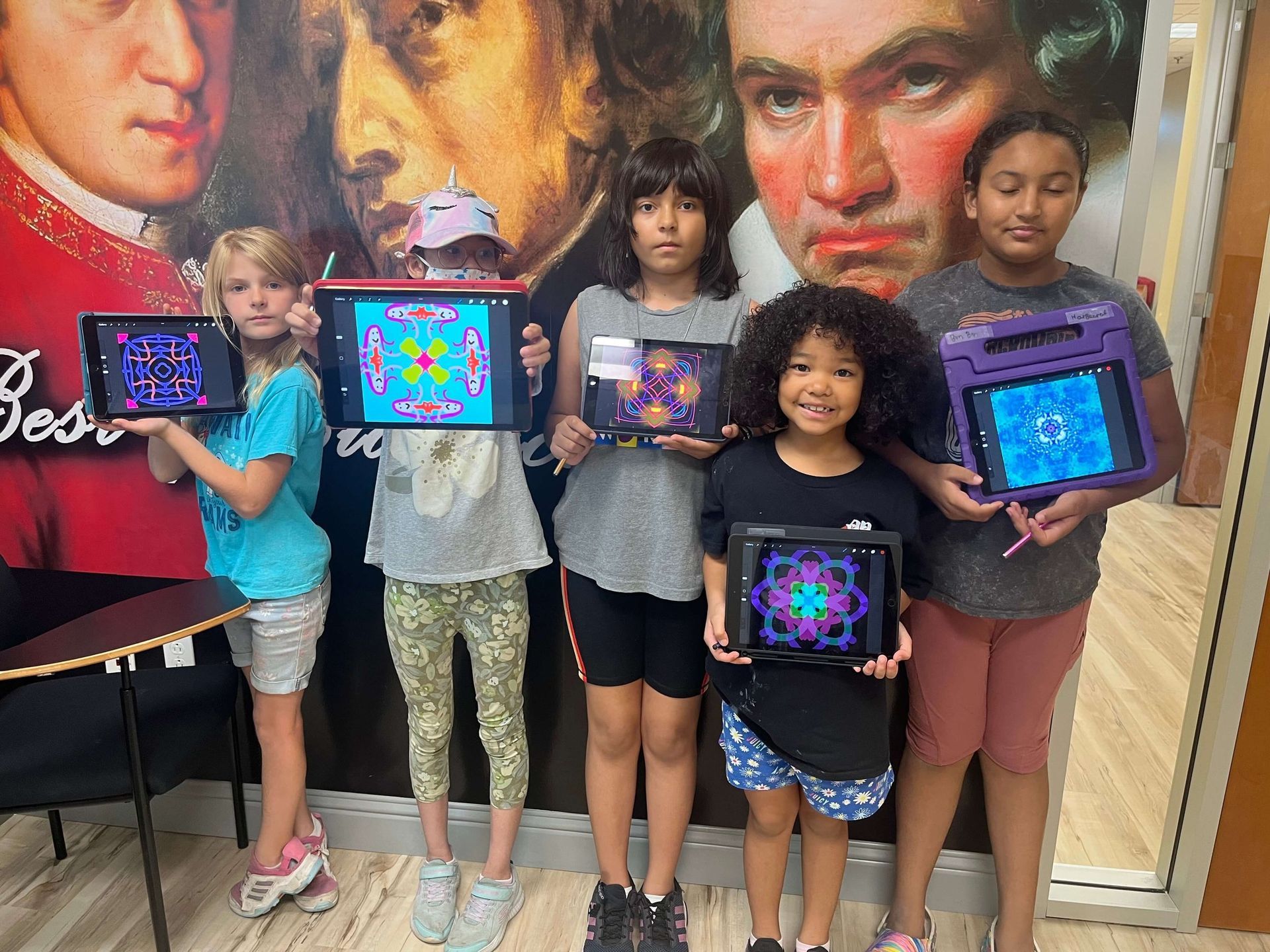 A group of young girls are holding up their tablets in front of a painting of beethoven.