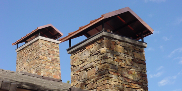 Two stone chimneys with copper roofs against a blue sky.
