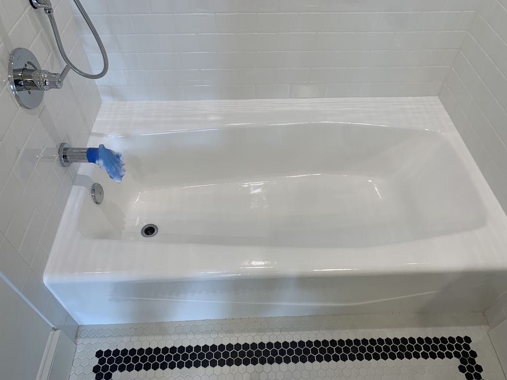 White bathtub with showerhead and blue bath sponge in a tiled bathroom.
