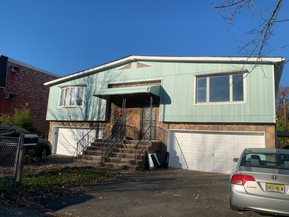 Split-level house with green siding, front steps, garage doors, and parked cars in the driveway