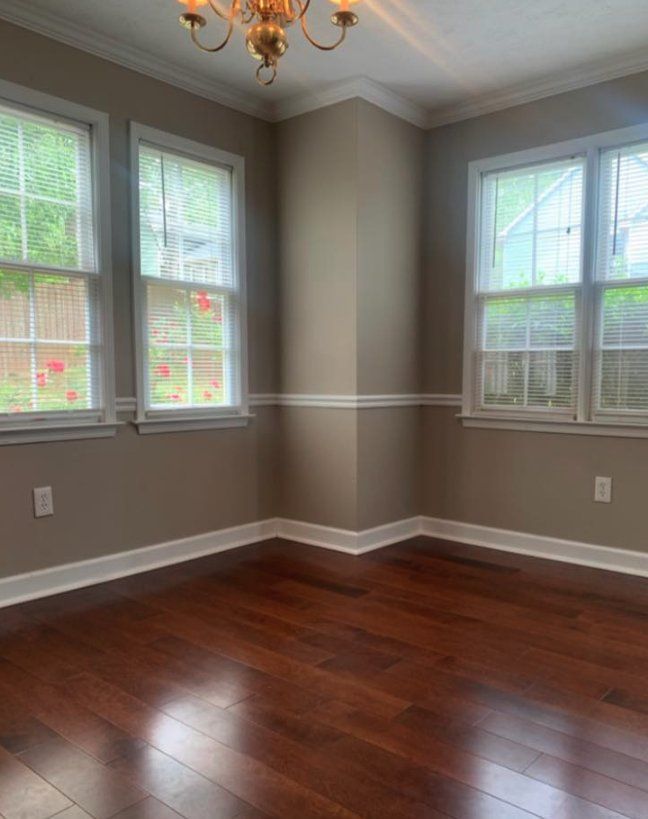 Empty room with dark hardwood floors, beige walls, white trim, and three tall windows