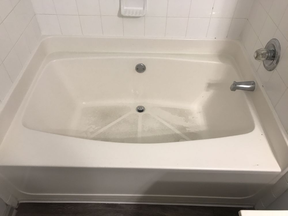White bathtub in a tiled bathroom, with showerhead, faucet, and drain visible.