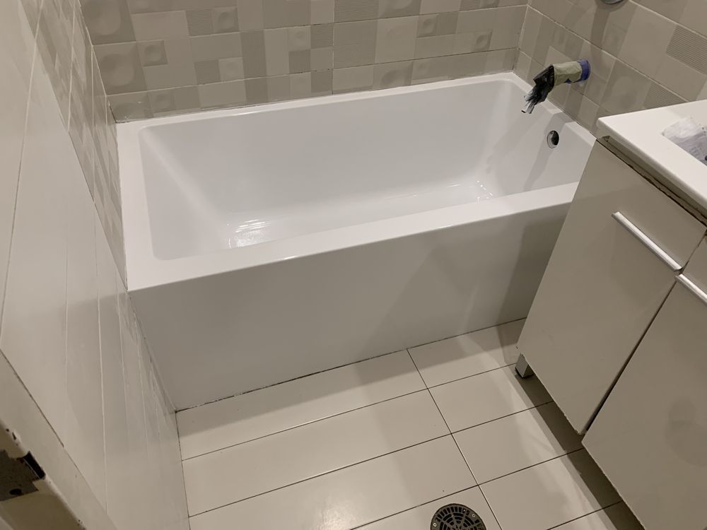 Small bathroom with a white bathtub, beige tile walls and floor, and a sink cabinet on the right.