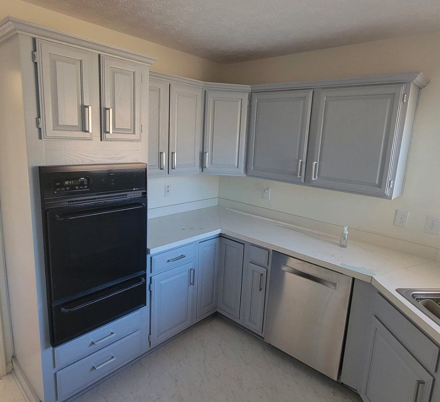 White L-shaped kitchen with gray cabinets, black oven, and stainless dishwasher in a bright corner layout