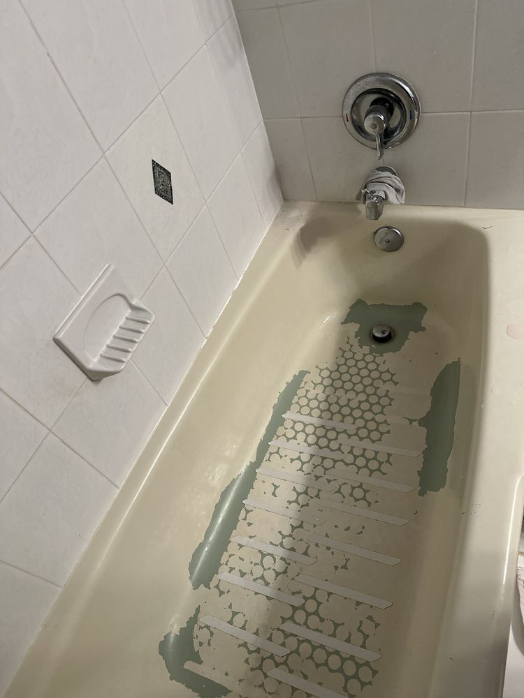 Empty bathtub with chipped, peeling paint and tiled walls underneath a chrome showerhead.