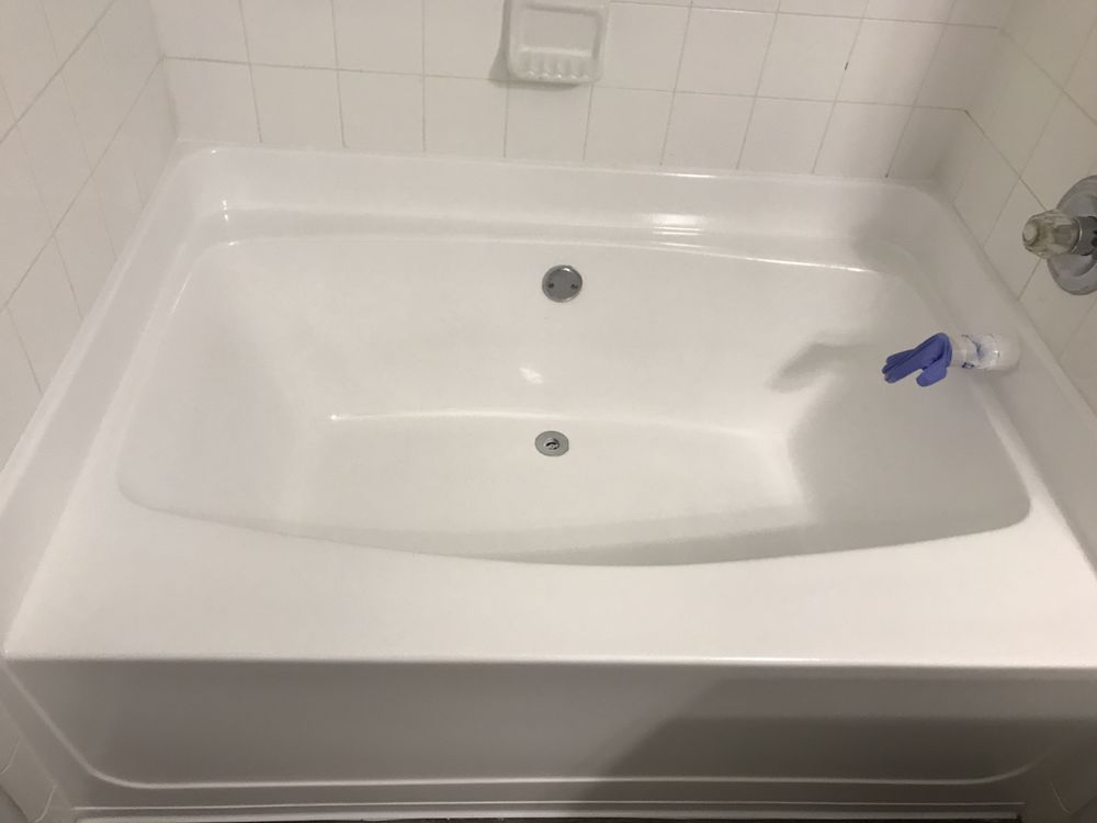 White bathtub in a tiled bathroom with a blue-and-white scrub brush on the rim.