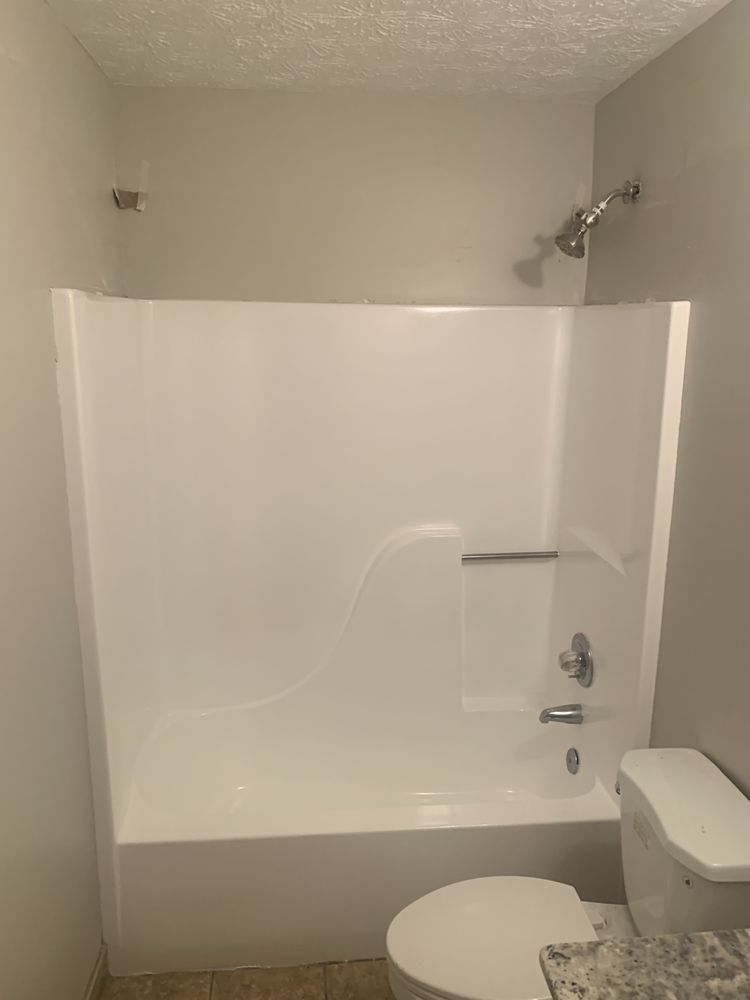 White bathtub shower enclosure with built-in seat, grab bar, and nearby toilet in a small bathroom