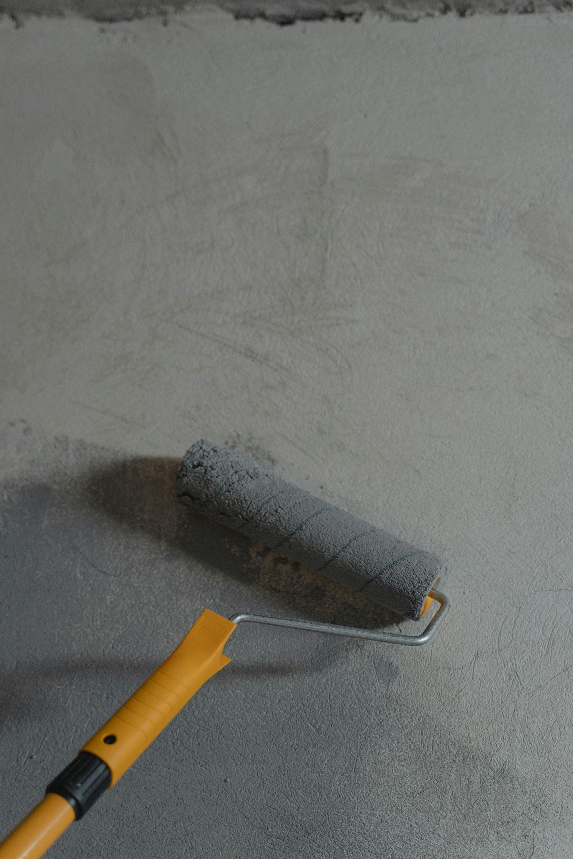Paint roller applying gray paint to a wall near the floor.