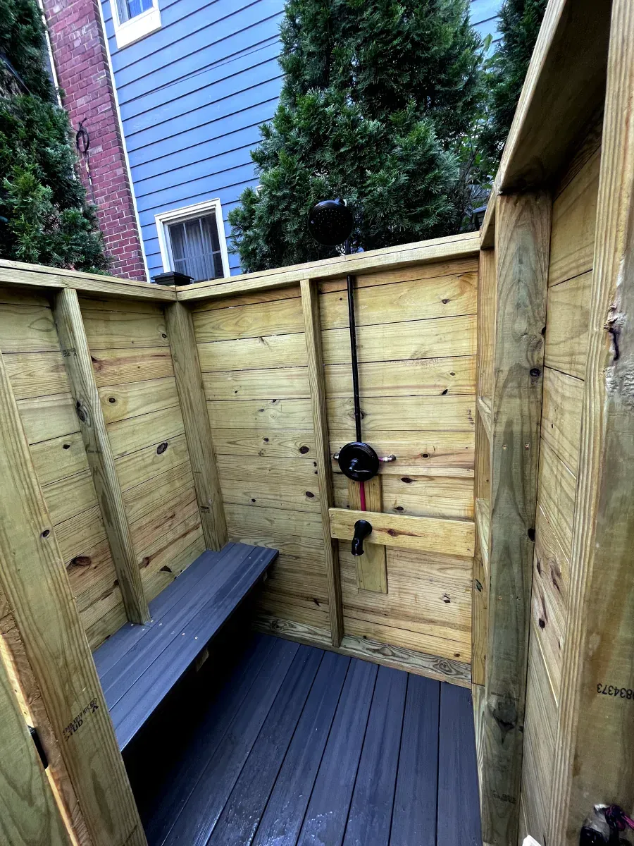 Outdoor wooden shower with bench and black fixtures.