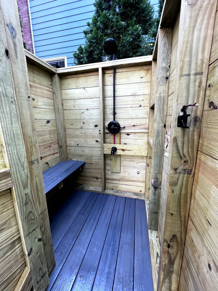 Outdoor wooden shower with a bench and dark gray flooring.