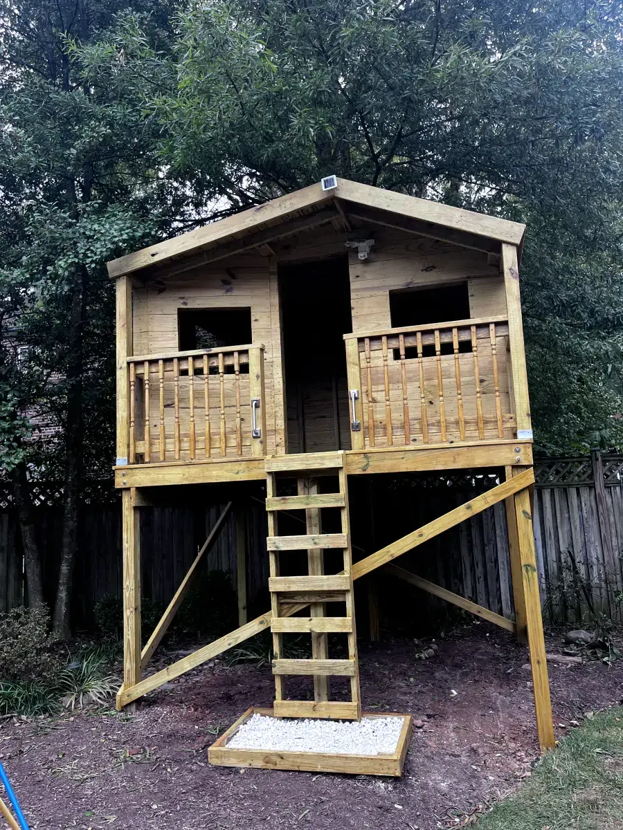 Wooden treehouse on stilts with ladder, front entrance, and two small windows.
