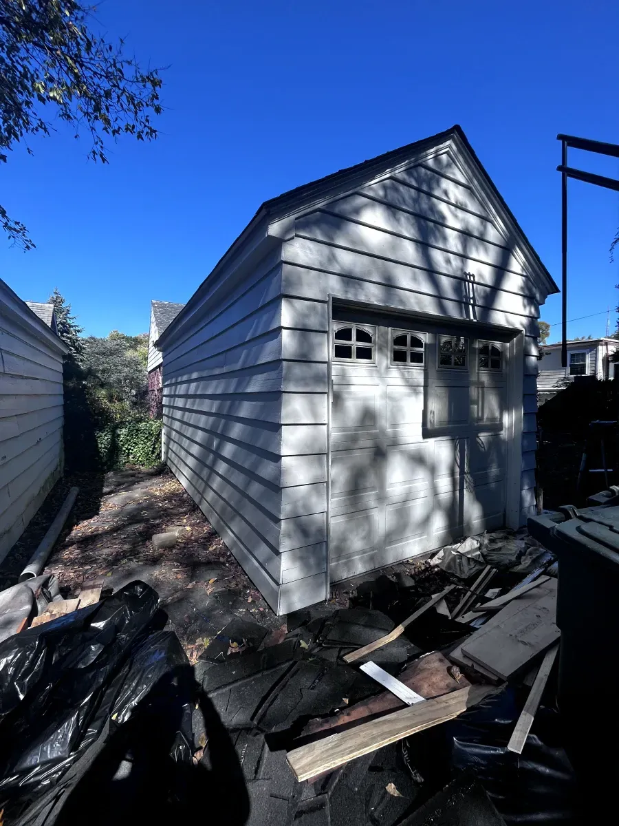 White clapboard garage under a clear blue sky, debris in foreground.