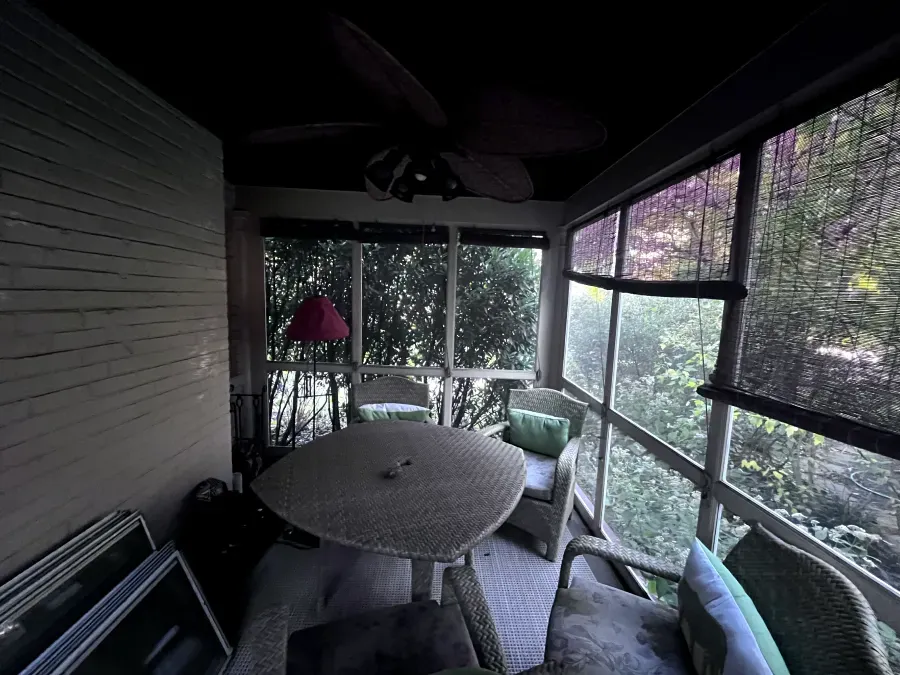 Screened porch with wicker furniture and view of trees.