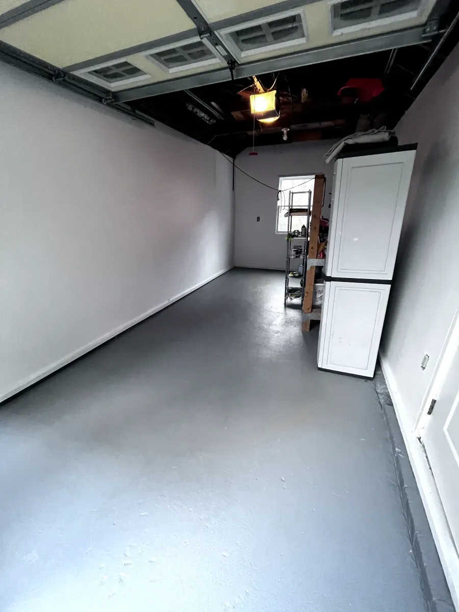 Empty garage with gray floor and white walls. White storage cabinets near the door.