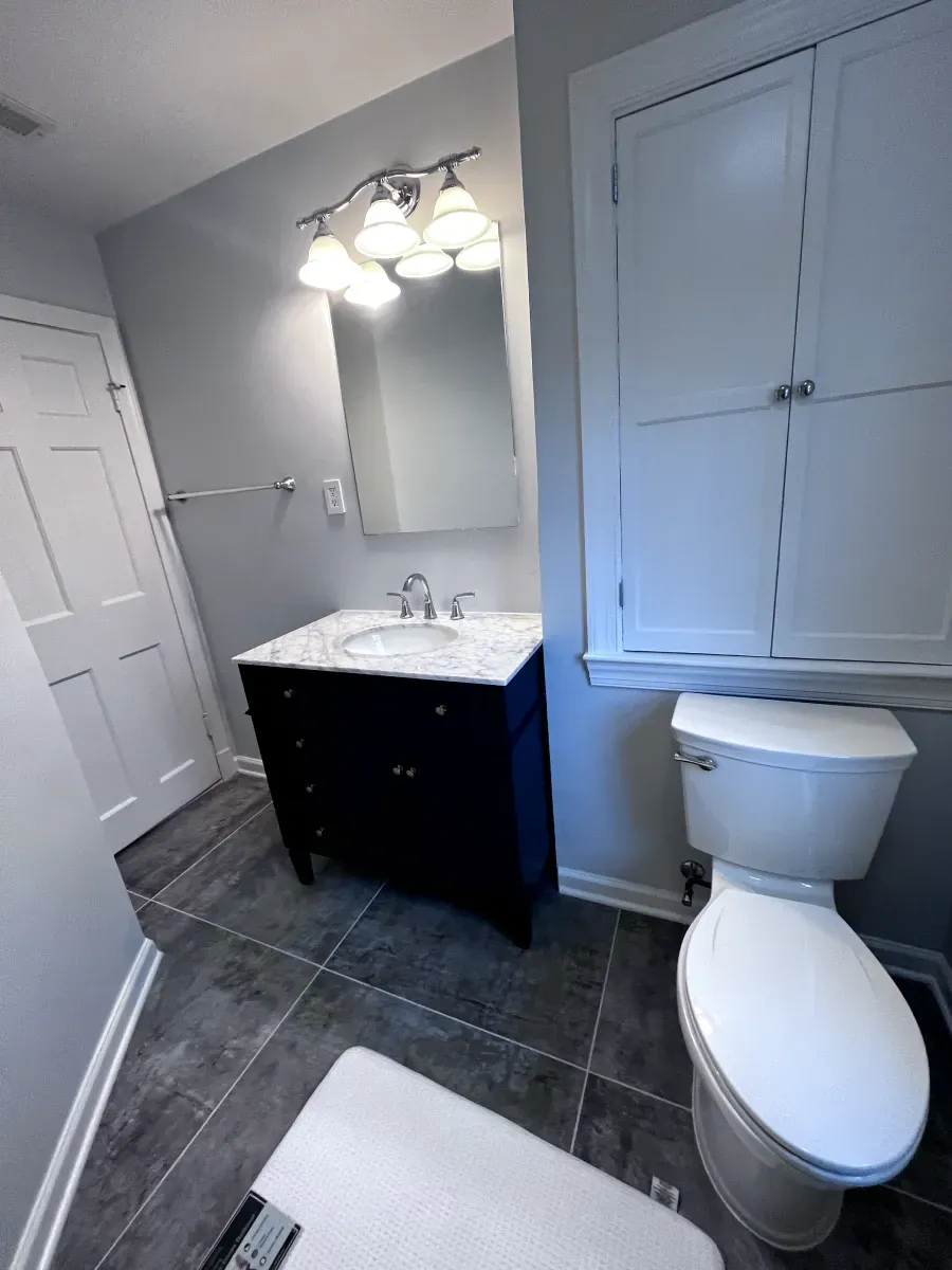 Bathroom with dark blue vanity, white countertop, and gray walls. White toilet and storage cabinet on the right.