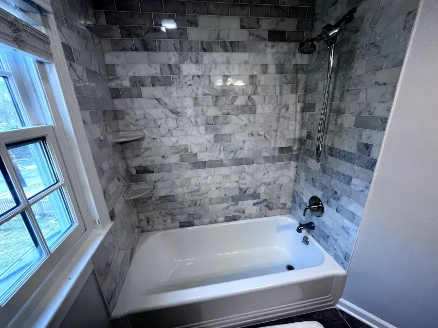 Bathroom with white tub, marble tile walls, shower, and window.
