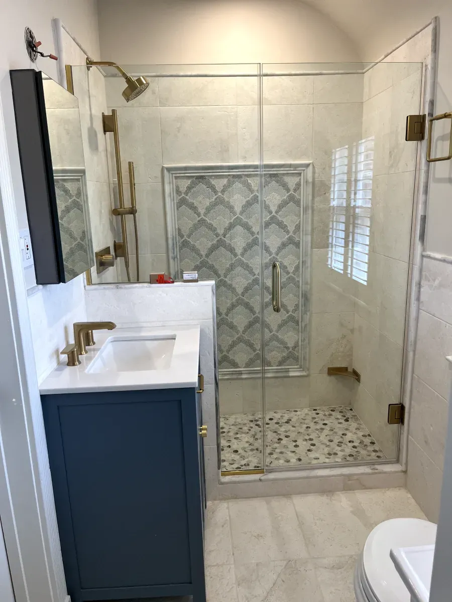 Small bathroom with blue vanity, glass shower, and patterned tile accents.