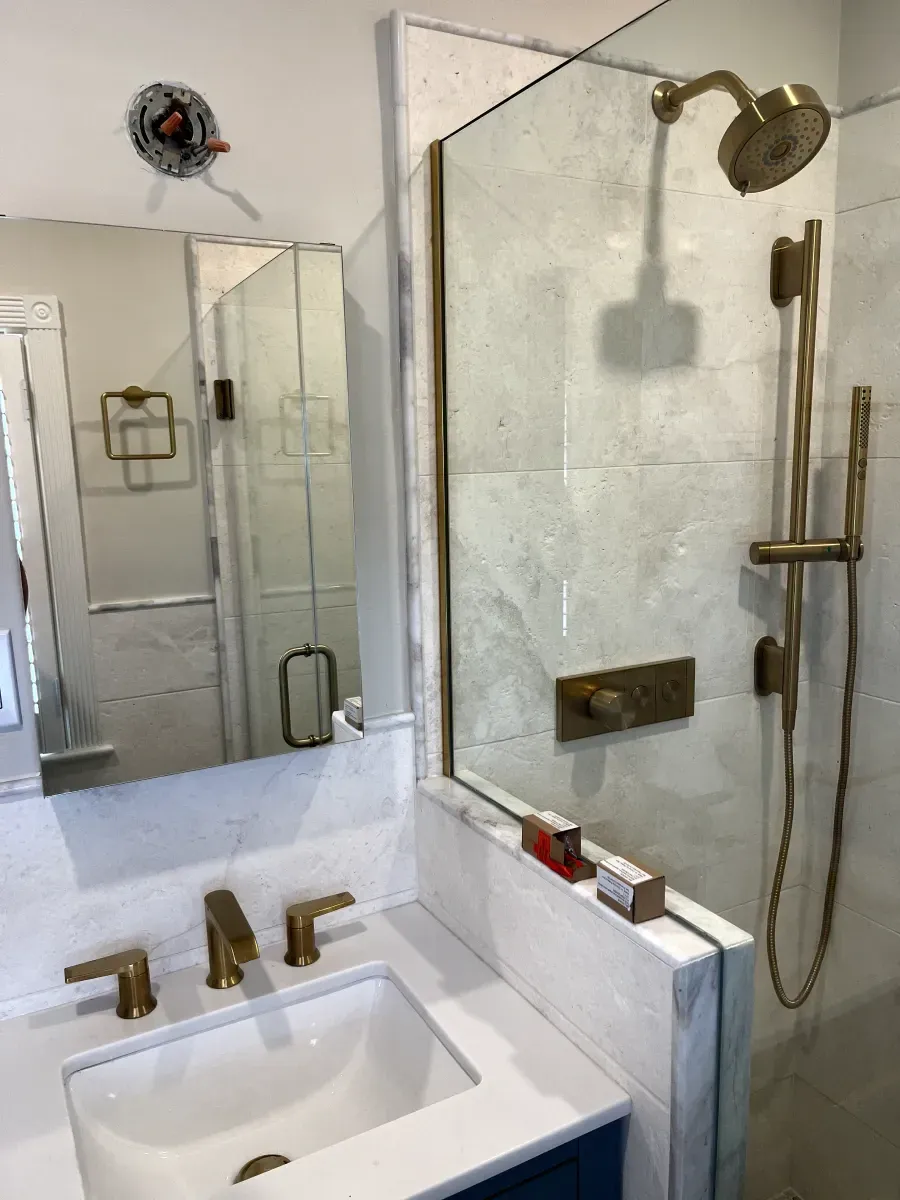 Bathroom with brass fixtures, white countertop, blue cabinet, and shower with glass enclosure.