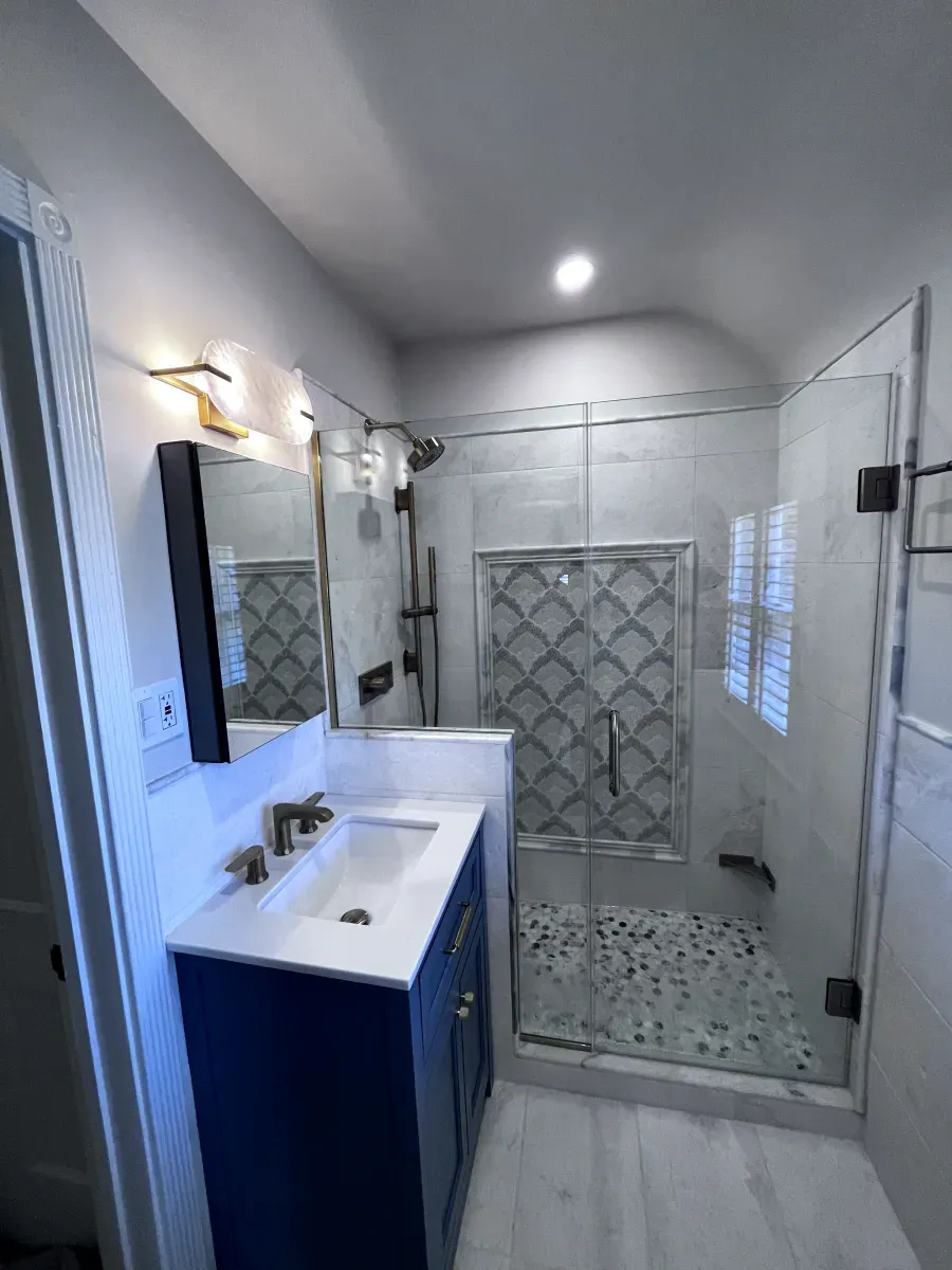 Modern bathroom with a navy blue vanity, glass shower, and white and gray tile.