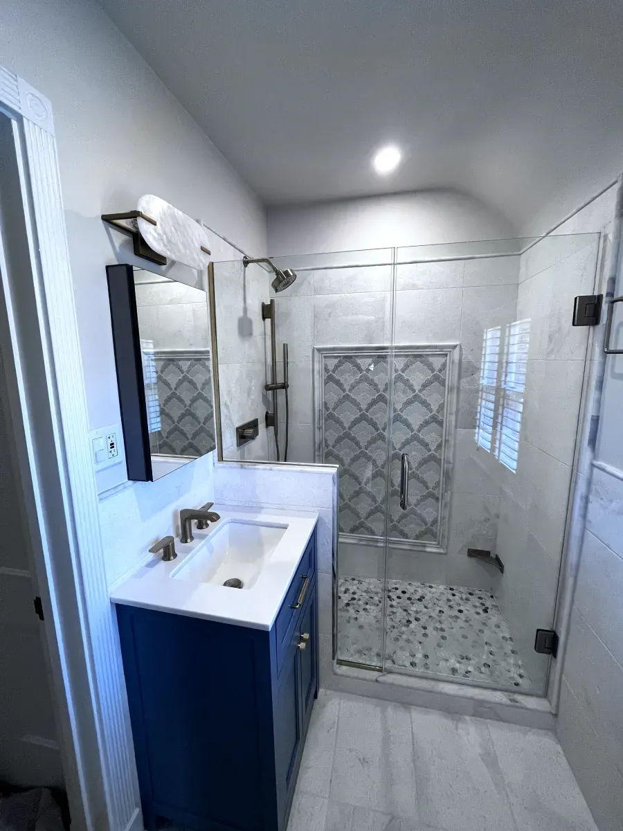 Modern bathroom with blue vanity, glass shower, and light-colored tile and walls.