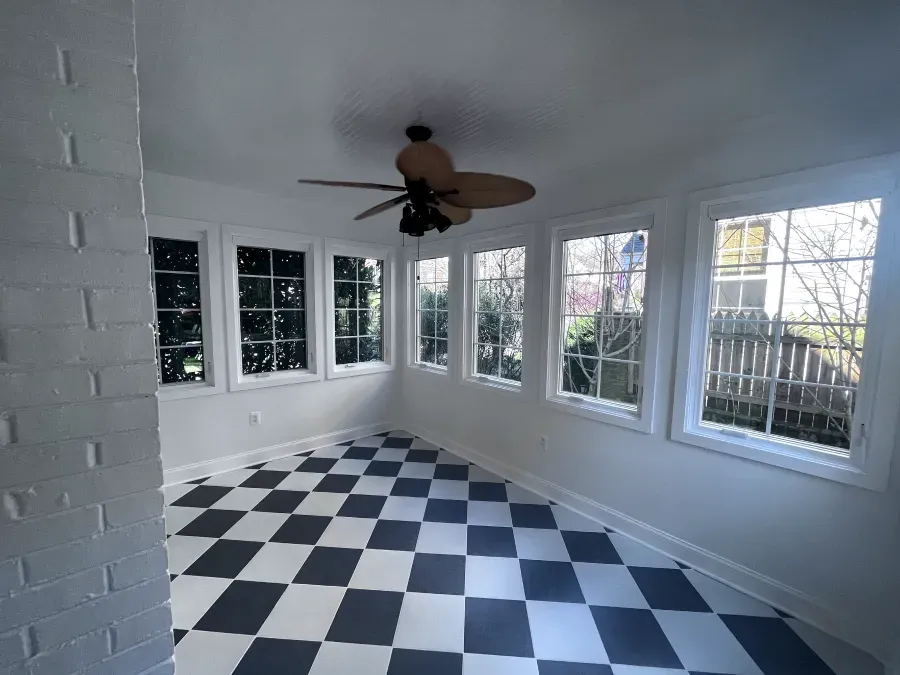 Sunroom with black and white checkered floor, windows, brick wall, and ceiling fan.