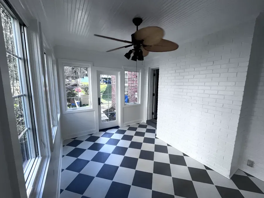 Sunroom with black and white checkered floor, white brick wall, and large windows.