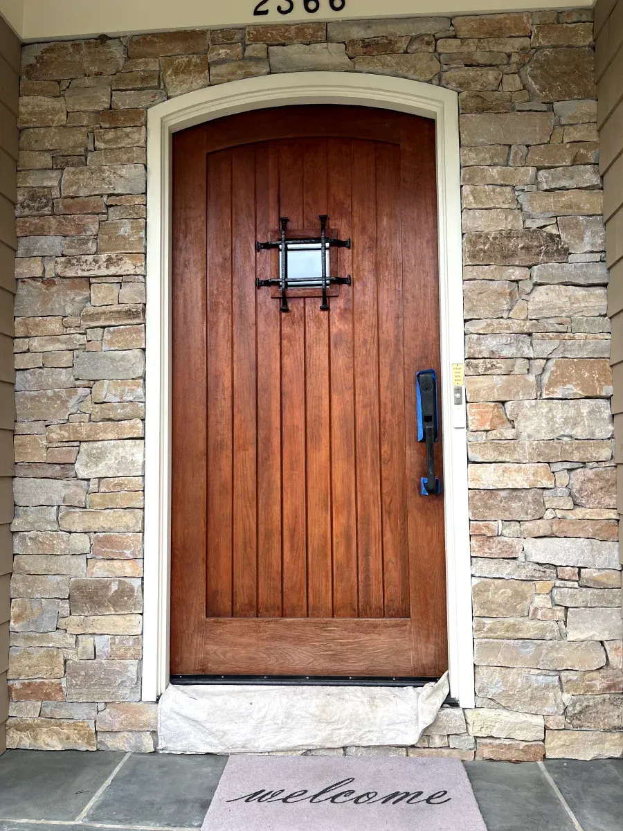 Wooden front door with iron grill, flanked by stone walls, 