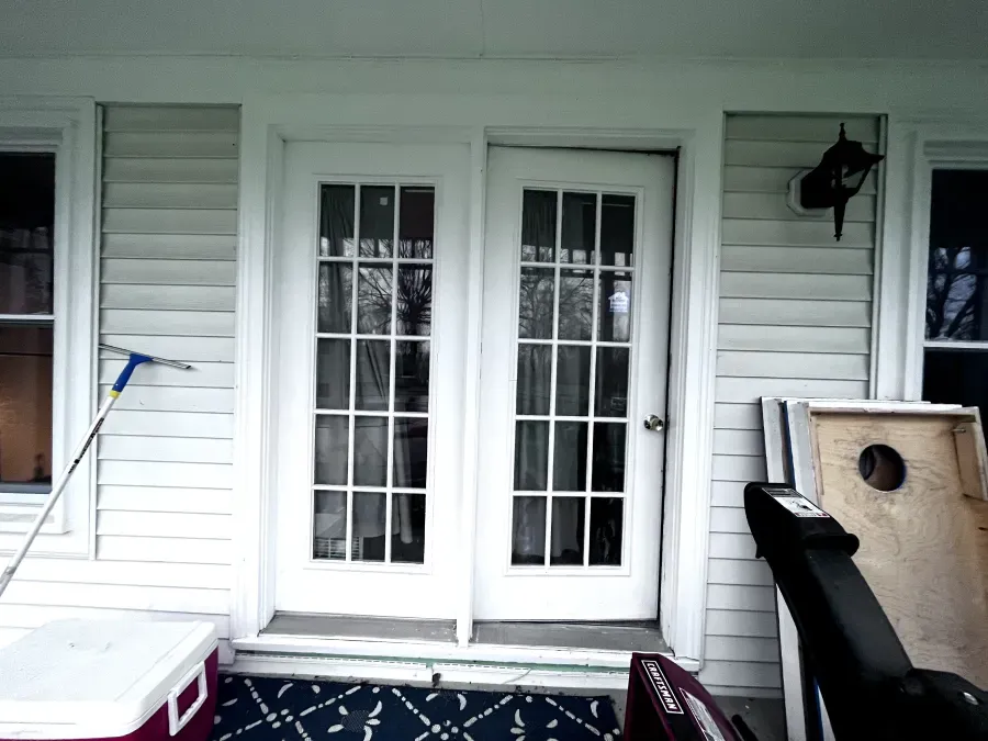 White French doors on a porch, flanked by windows, with a cooler and other items nearby.