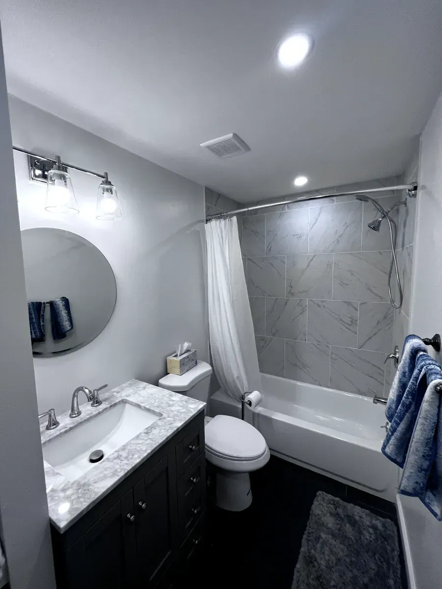Bathroom with a gray vanity, round mirror, toilet, tub, and shower.