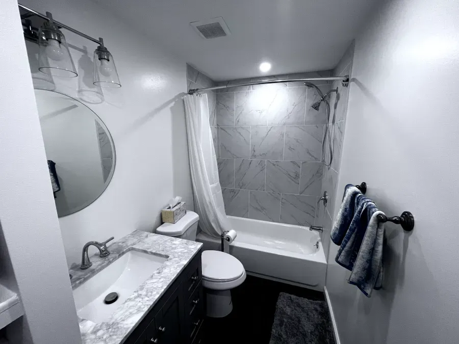Modern bathroom with white walls, shower/tub, vanity, toilet, and circular mirror.