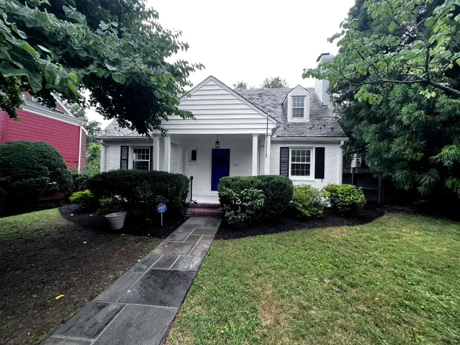 White house with blue door, stone walkway, and green bushes and lawn.