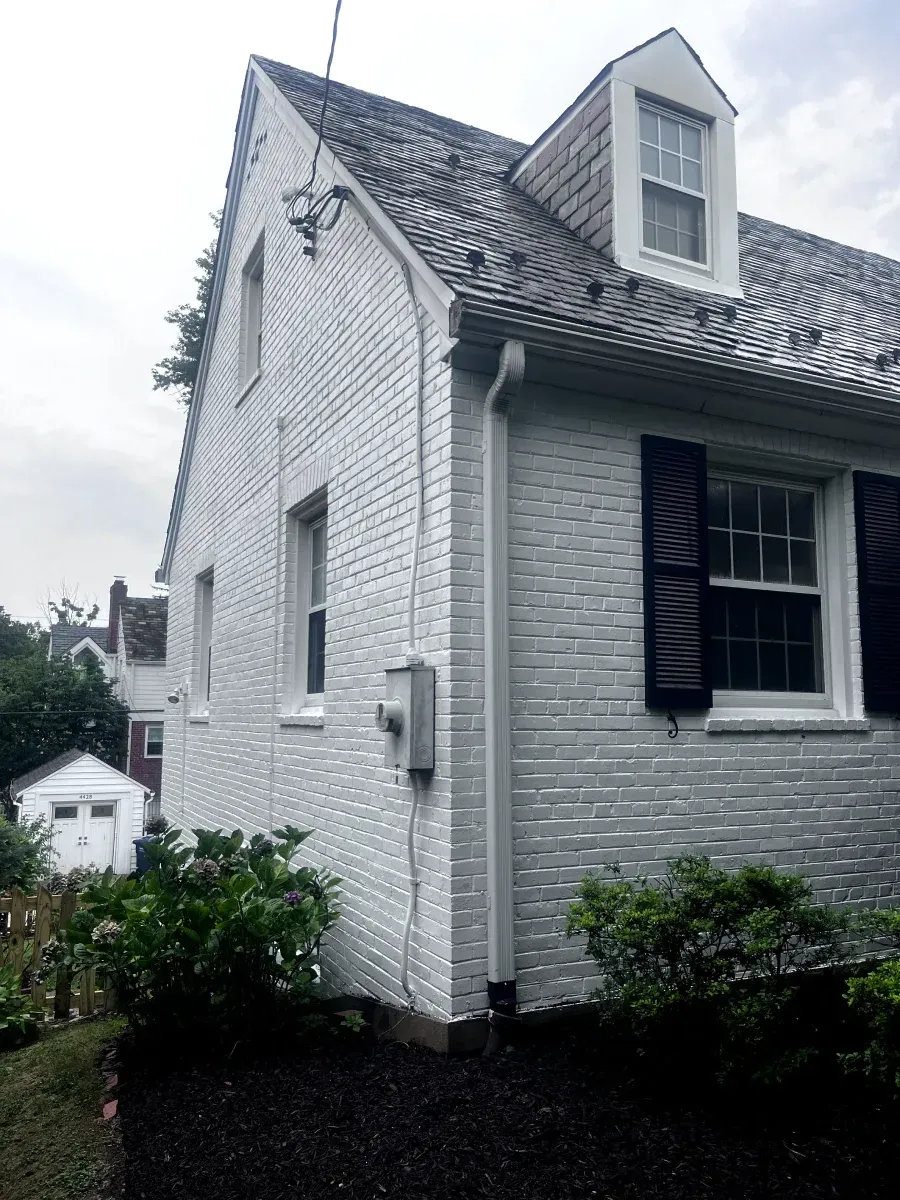 White brick house with black shutters and dark roof. Landscaping with black mulch.
