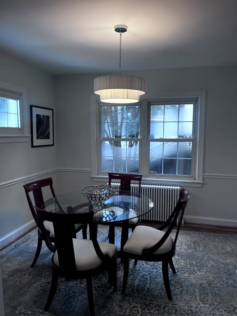 Dining room with round glass table, four chairs, rug, and a tiered chandelier.
