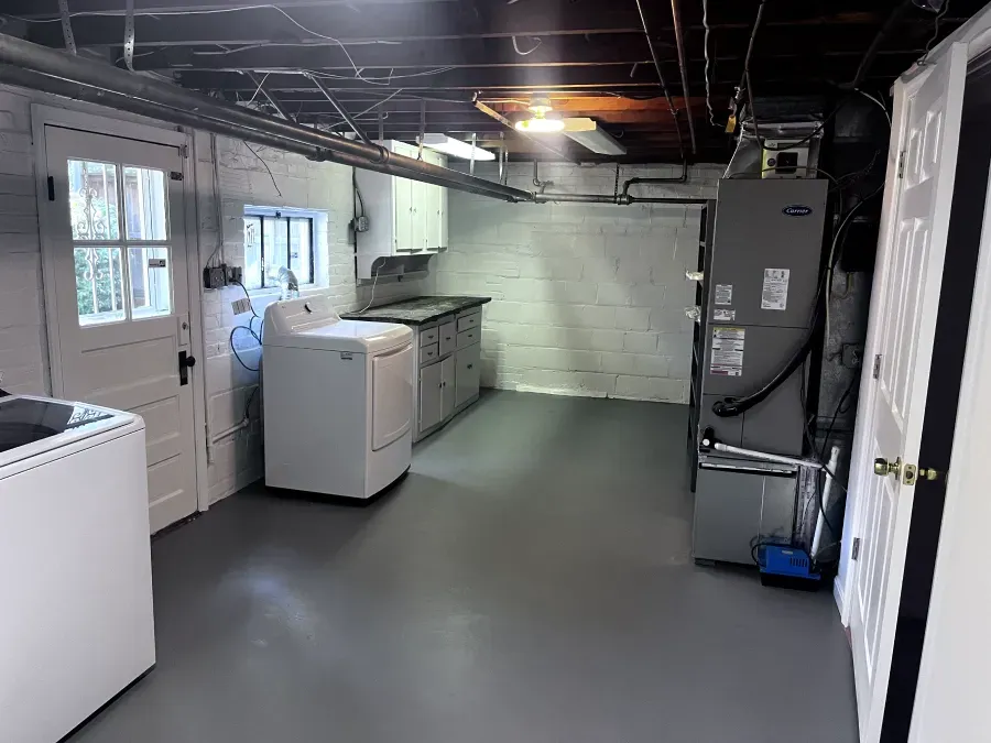 Laundry room with a washing machine, dryer, and utility sink, with gray flooring and white walls.
