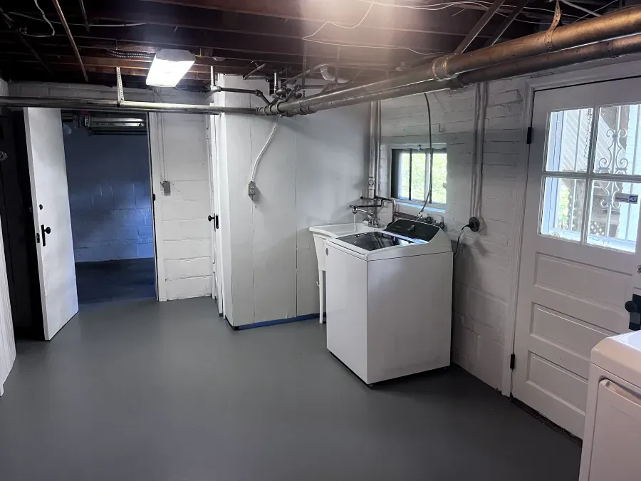 Basement laundry room with white washer, doors, gray floor, and a small window.