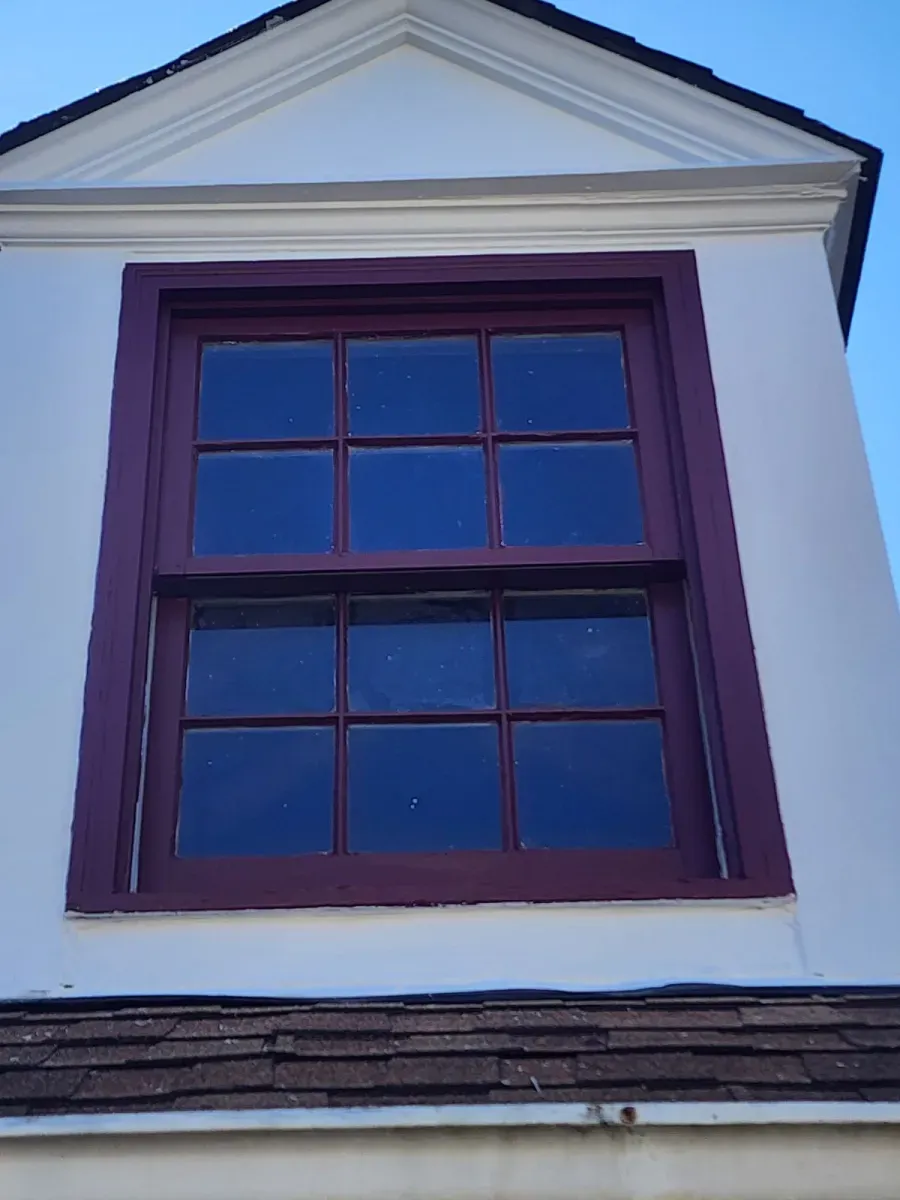 Tall window with burgundy trim on white building, against a blue sky.